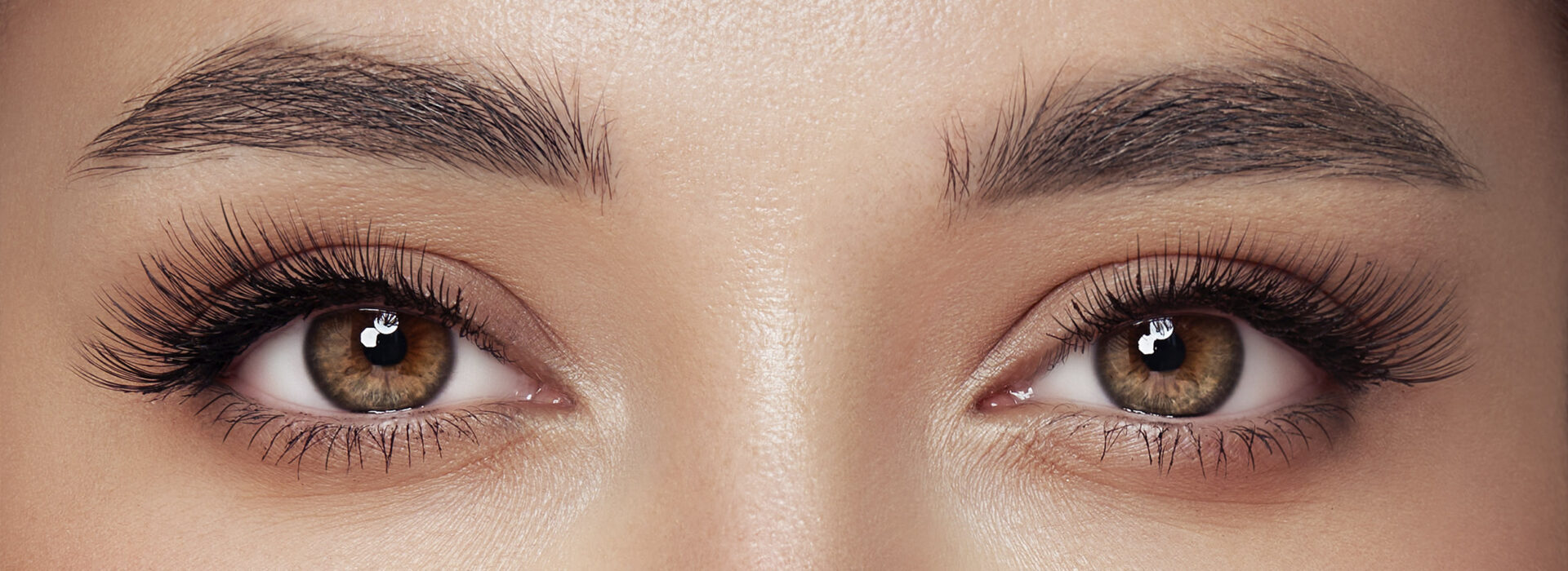 Dois olhos de uma mulher olhando para frente. A imagem foca em sua sobrancelha e cílios.